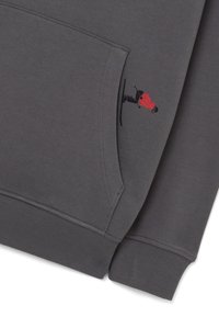 Grijze sweatshirt met een klein rood geborduurd figuur op het zakgebied, met ribboorden bij de mouwen en onderkant voor extra textuur.