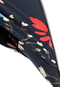 Gros plan d’un tissu foncé avec des motifs floraux rouges, blancs et bleus et des tiges verdâtres sur une section pliée.