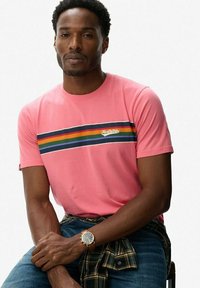 Roze katoenen t-shirt met een horizontaal streepdessin in zwart, groen, geel en blauw. Opvallende details zijn een logo en een aansluitende pasvorm.