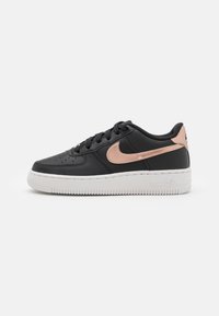 Crne kožne tene s metalik ružičasto zlatnim Nike swooshom, bijelim gumenim potplatom, okruglim vrhom i teksturiranim detaljima na gornjem dijelu.