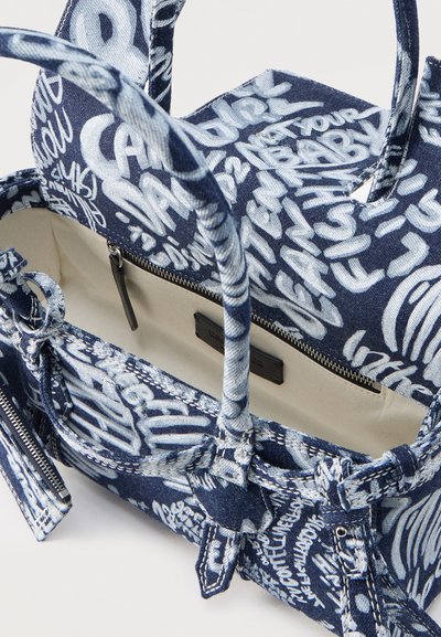 Sac fourre-tout en tissu bleu avec texte en style graffiti blanc, ouverture supérieure montrant un intérieur beige avec poche zippée et doubles poignées.