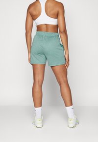 Shorts de entrenamiento color teal claro con cintura elástica y bolsillos laterales, combinados con un sujetador deportivo blanco y zapatillas con detalles en neón.