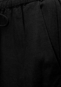 Pantalon en lin noir avec une taille à cordon de serrage et des poches latérales, présentant une surface de tissu lisse mais légèrement texturée.