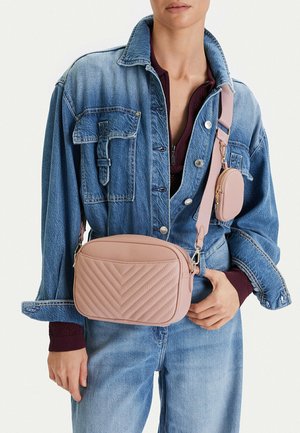 Person trägt blaue Jeansjacke und Jeans mit einer gesteppten rosa Umhängetasche und einer passenden kleinen Tasche am Riemen.