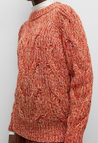 Roter und oranger gestrickter Pullover mit Rundhalsausschnitt, der Kabelmuster sowie einen gerippten Saum und Bündchen aufweist und eine strukturierte Oberfläche zeigt.
