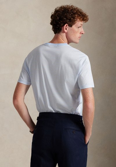 Ανοιχτό μπλε ριγέ κοντομάνικο t-shirt με στρογγυλή λαιμόκοψη, κατασκευασμένο από μαλακό ύφασμα. Συνδυάζεται με σκούρο ναυτικό μπλε παντελόνια με πίσω τσέπες.