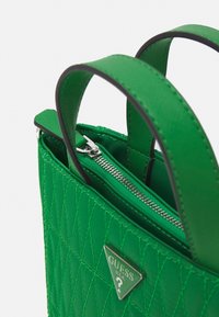 Vihreä tikattu käsilaukku keinomateriaalista, hopeanvärisillä metalliosilla, vetoketjulla ja kahdella kahvalla. Logo kolmion muotoinen korostus edessä.