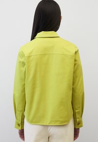 Jasnozielona kurtka z kołnierzem, długimi rękawami i zapięciem na guziki. Gładki materiał o prostym kroju i lekko zaokrąglonym dole.