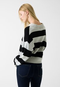 Pull à col rond avec des rayures audacieuses alternant noir et gris clair. Matière en maille douce avec une coupe décontractée et un ourlet côtelé.