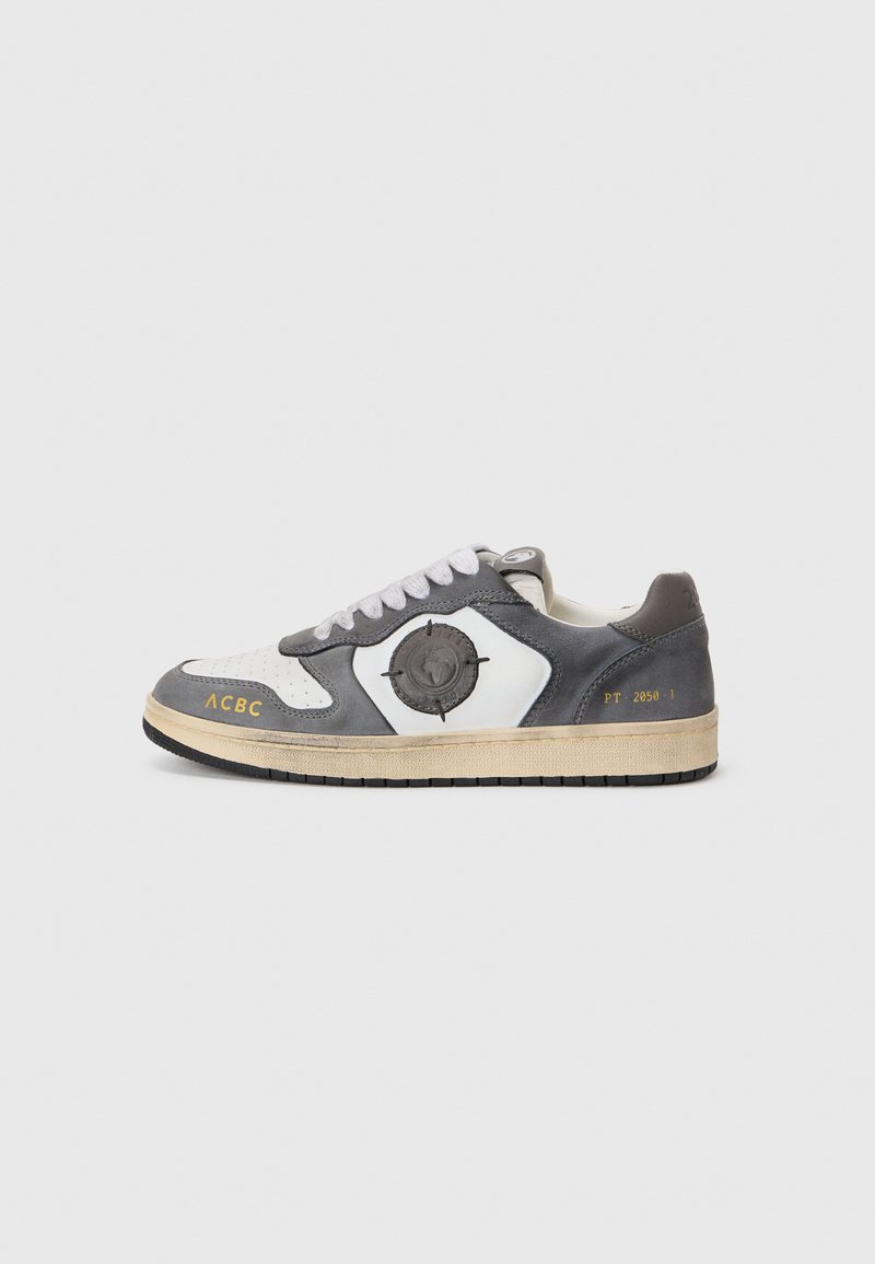 Sapatilhas cinzas e brancas com um design texturizado, apresentando um logotipo circular, atacadores brancos, sola em contraste e detalhes impressos na lateral.