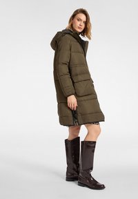 Długa, oliwkowozielona pikowana kurtka z kapturem, z poziomymi przeszyciami, dwoma przednimi kieszeniami i suwakiem. Noszona z wysokimi, ciemnobrązowymi kozakami.