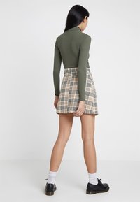 Top ajustado de manga larga verde oliva combinado con una falda mini de cuadros beige. Zapatillas negras con cordones y calcetines blancos hasta el tobillo completan el atuendo.