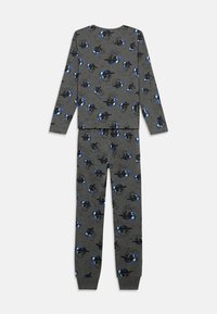 Temno siva majica z dolgimi rokavi in hlače z vzorcem ponavljajočih se modrih in črnih lobanj, ki nosijo kapo in slušalke.