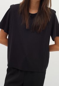 Svart kortärmad t-shirt i mjuk bomull, med en lös passform och enkel rund halsringning. Minimalistisk design utan synliga mönster.