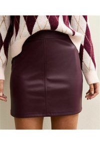 Mini-jupe en similicuir bordeaux avec une texture lisse et des coutures verticales, associée à un pull en maille à motif.