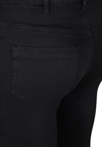 Zbliżenie na czarne dżinsy pokazujące tylną kieszeń, szlufkę na pasek oraz detale przeszyć na dopasowanym ubraniu.