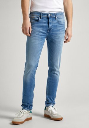 Jeans de mezclilla azul claro con corte ajustado, que presentan un diseño clásico de cinco bolsillos y un ligero desvanecimiento. Combinados con zapatillas blancas.