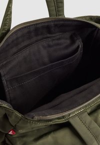 Maslinasto zelena torba s patentnim zatvaračem, s crnim unutarnjim materijalom i malim džepom, koja prikazuje izdržljive materijale i šavove.