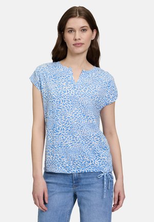 Top bleu à manches courtes avec encolure en V, présentant un motif abstrait texturé dans des nuances de bleu variées et un ourlet à cordon de serrage.