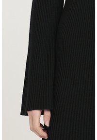 Svart ribbad tröja med långa ärmar och ett utsvängt manschettdesign som framhäver en mjuk textur och väldefinierade vertikala linjer.