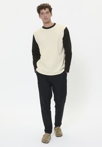Lichtcreme lange mouwen bovenstuk met zwarte mouwen, gecombineerd met donker trousers en beige instappers. Soepele textuur; comfortabele pasvorm.