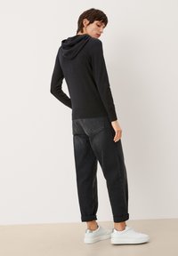 Czarny hoodie z organicznej bawełny o luźnym kroju, z ribbowanymi mankietami i dołem. Połączony z ciemnymi dżinsami i białymi trampkami z srebrnymi akcentami.