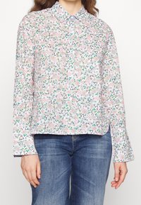 Chemise florale à manches longues, avec un motif rose, vert et blanc sur un tissu léger. Col à revers et coupe ample.