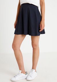Granatowa spódnica dżokejka wykonana z bawełny, o rozkloszowanym kroju i gładkiej fakturze. Stylizowana z białą bluzką i białymi tenisówkami.