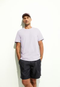 T-shirt en coton lavande à manches courtes, associée à un short sombre. Une casquette lavande assortie complète le look décontracté.