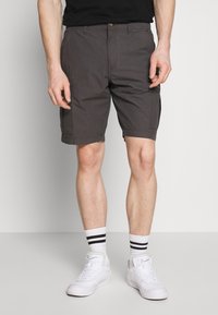 Shorts cargo gris foncé avec plusieurs poches, une fermeture à bouton et une coupe droite. Portés avec des baskets blanches et des chaussettes à rayures noires.