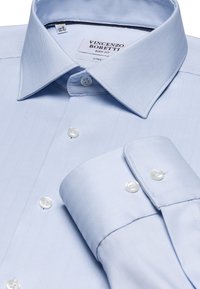 Lichtblauw overhemd met visgraatpatroon, button-down kraag en placket. Voorzien van witte knopen en een manchet met een gladde afwerking.