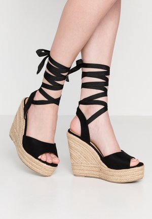 Černé platformové sandály s přírodní šňůrkovou podešví, otevřenou špičkou a křížovými černými stužkami omotávajícími kotník.