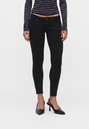 Femme portant un jean skinny noir, des talons hauts noirs pointus et un haut à manches longues rayé noir et gris raccourci à la taille.
