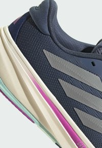 Marineblauwe sportschoen met een gestructureerde bovenkant, metallic grijze strepen, gelaagde zool in roomkleur met turquoise en paarse accenten.