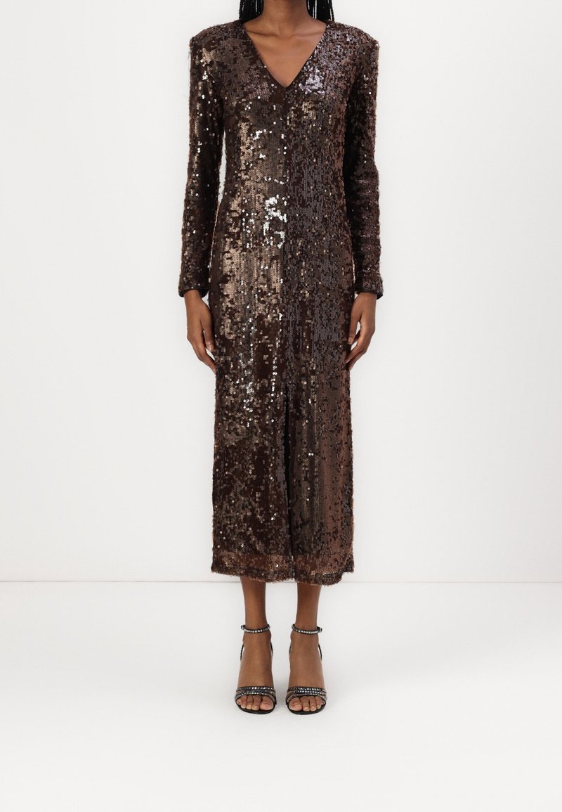 Personne portant une robe midi à manches longues, marron foncé à sequins, avec un décolleté en V et une fente à l'avant, associée à des escarpins noirs à brides à la cheville.