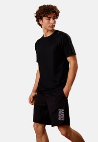 Sort atletisk T-shirt med korte ærmer og rund halsudskæring, parret med sorte shorts med et reflekterende 'RUN'-logo på siden.