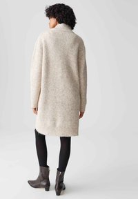 Abito maglione in beige con texture a coste, maniche lunghe e colletto alto, abbinato a leggings neri e stivali ankle brown.
