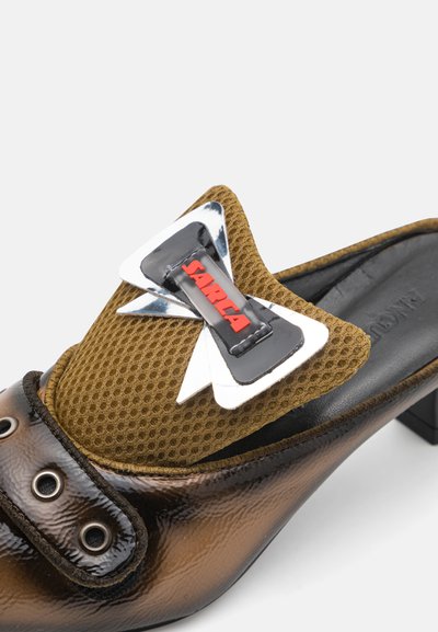 Zapato de tacón marrón y negro con parte superior de malla, que presenta un gran lazo en cromo y rojo. Punta redondeada y detalle decorativo en hardware.