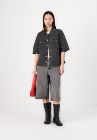 Čierna denimová oversized košela bunda s krátkymi rukávmi, skombinovaná so šedými culottes, čiernymi vysokými čižmami a červenou kabelkou.