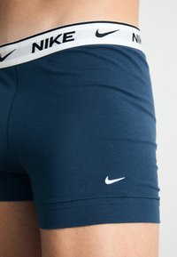 Tamno plave Nike gaće sa kontrastnom bijelom elastikom koja sadrži naziv brenda i logo. Glatka tekstura s prilagođenim dizajnom.