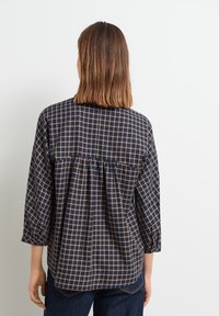 Blouse marine avec un motif à carreaux beige, manches trois-quarts, dos froncé et coupe décontractée. Tissu lisse et léger.