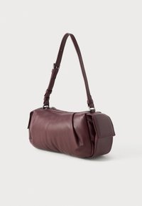 Sac à main en cuir bordeaux de forme arrondie, avec une bandoulière réglable et des détails texturés. Il possède une fermeture à rabat sur un côté.