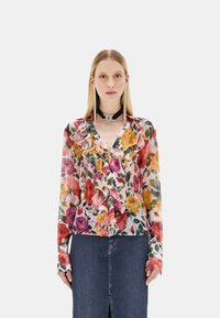 Blusa floreale in tessuto trasparente con parte anteriore arricciata, caratterizzata da fiori rossi, rosa e gialli su uno sfondo chiaro; maniche lunghe e chiusura con bottoni.