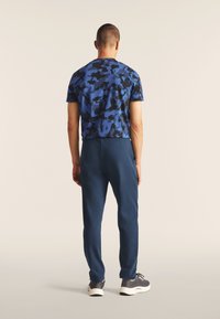 Camisa de manga corta de camuflaje azul con acentos negros, combinada con joggers de color marino sólidos. El conjunto presenta un corte relajado y un diseño casual.