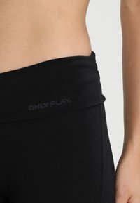 Crne sportske tajice s širokim, preklopnim pojasom na kojem je suptilno otisnuto ime branda "ONLY PLAY". Glatka tekstura, prilagođen oblik.