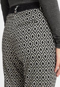 Schwarz-weiße gemusterte Hosen weisen ein Diamantdesign auf, mit einer glatten Textur und einem elastischen Bund, der mit "FEEL GOOD" beschriftet ist.