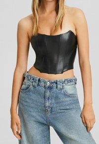 Svart fusk läder bustier topp med en strukturerad design och vertikala sömdetaljer, ihop med högmidjade ljusblå denimjeans.