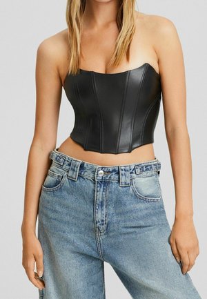 Top de bustier de cuero sintético negro con un diseño estructurado y detalles de costura vertical, combinado con jeans de mezclilla de tiro alto en un tono azul claro.