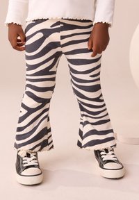 Zebra-stribede, ribbede flared bukser i sort og hvid, med en tekstureret finish og frynset kant, stylet med sorte sneakers.