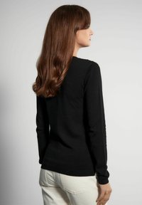 Czarny sweter z długim rękawem o dopasowanym kroju, miękkiej fakturze i starannym przeszyciu na ramionach, zestawiony z jasnymi spodniami.